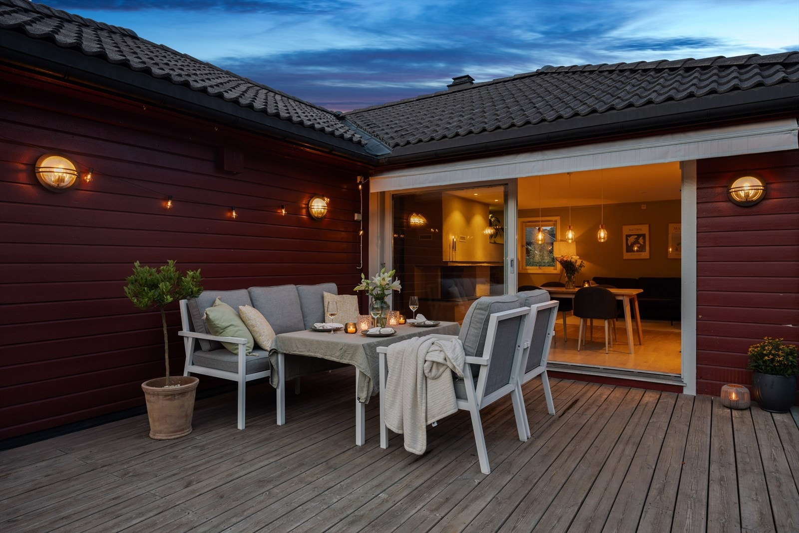 Store vindusflater gir en fin sammenheng mellom inne og ute, og lar lyset fra stuen skape en varm og innbydende stemning utendørs. Galleribilde