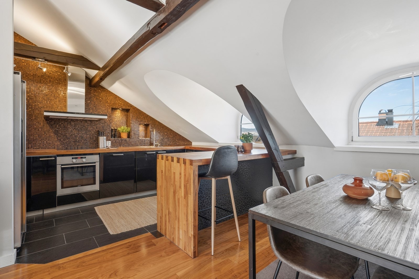 Kjøkkenet ligger i åpen løsning mot stuen og fremstår som delikat og funksjonelt, med sorte, slette høyglansfronter og heltre eikebenkeplate som tilfører varme og karakter. Galleribilde