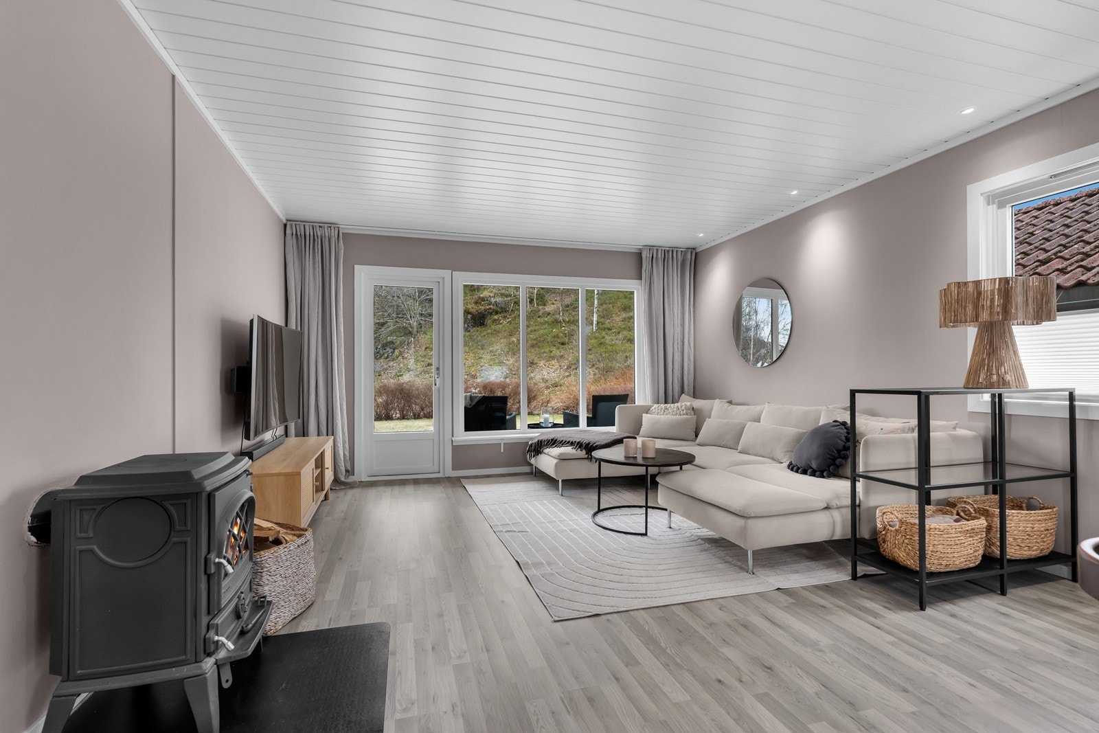 Innvendig er leiligheten delikat innredet i lyse og pene farger - her fra stuen med peisovn og utgang til terrasse/hage Galleribilde