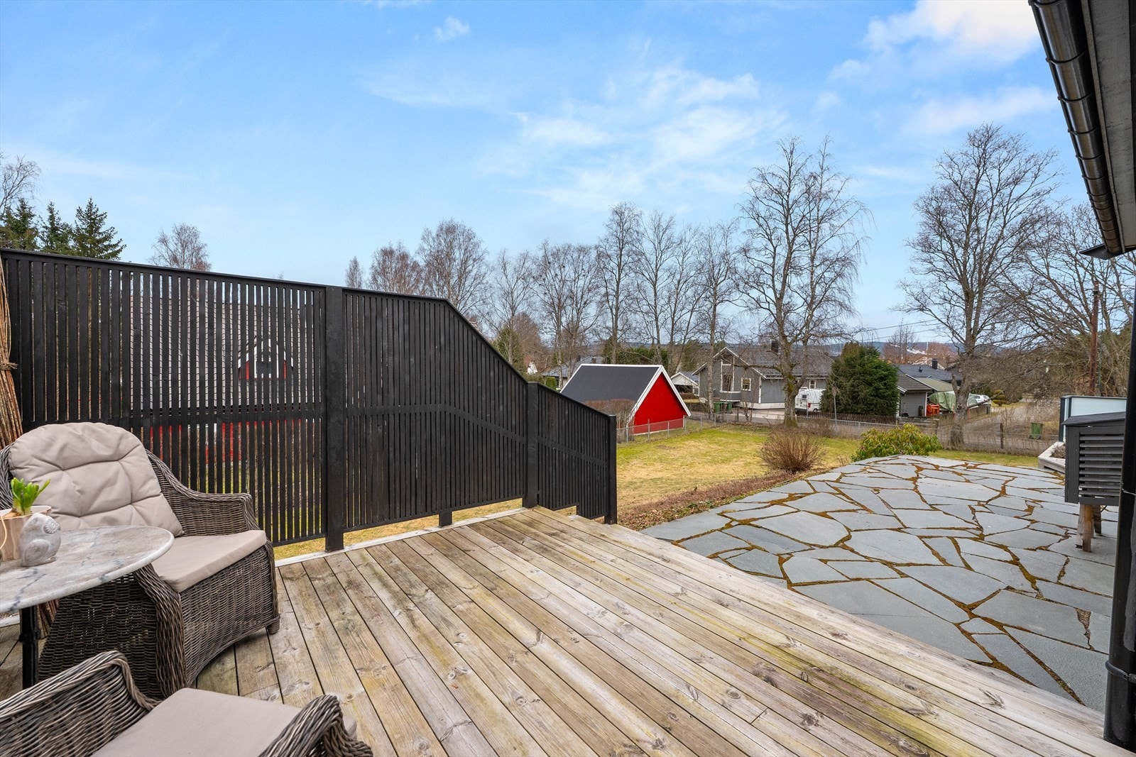 Tomten er pent opparbeidet med en kombinasjon av treterrasse, skiferheller og plen. Galleribilde