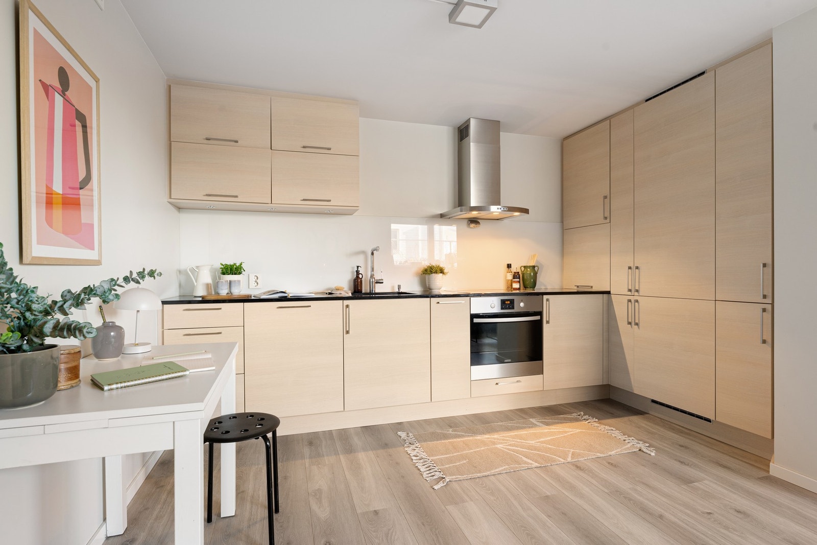 Kjøkkeninnredningen har en funksjonell og plassbesparende utforming, med glatte fronter og gode oppbevaringsmuligheter i skap og skuffer. Det er opplegg for platetopp, stekeovn, oppvaskmaskin og kombi kjøl/fry. Galleribilde
