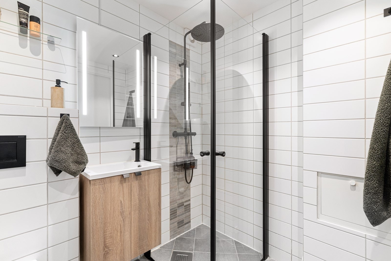 Badet fremstår som praktisk med veggmontert toalett, dusjhjørne med inn- og utadslående dusjvegger, en stilfull servant med ettgreps blandebatteri i møbelinnredning. Galleribilde