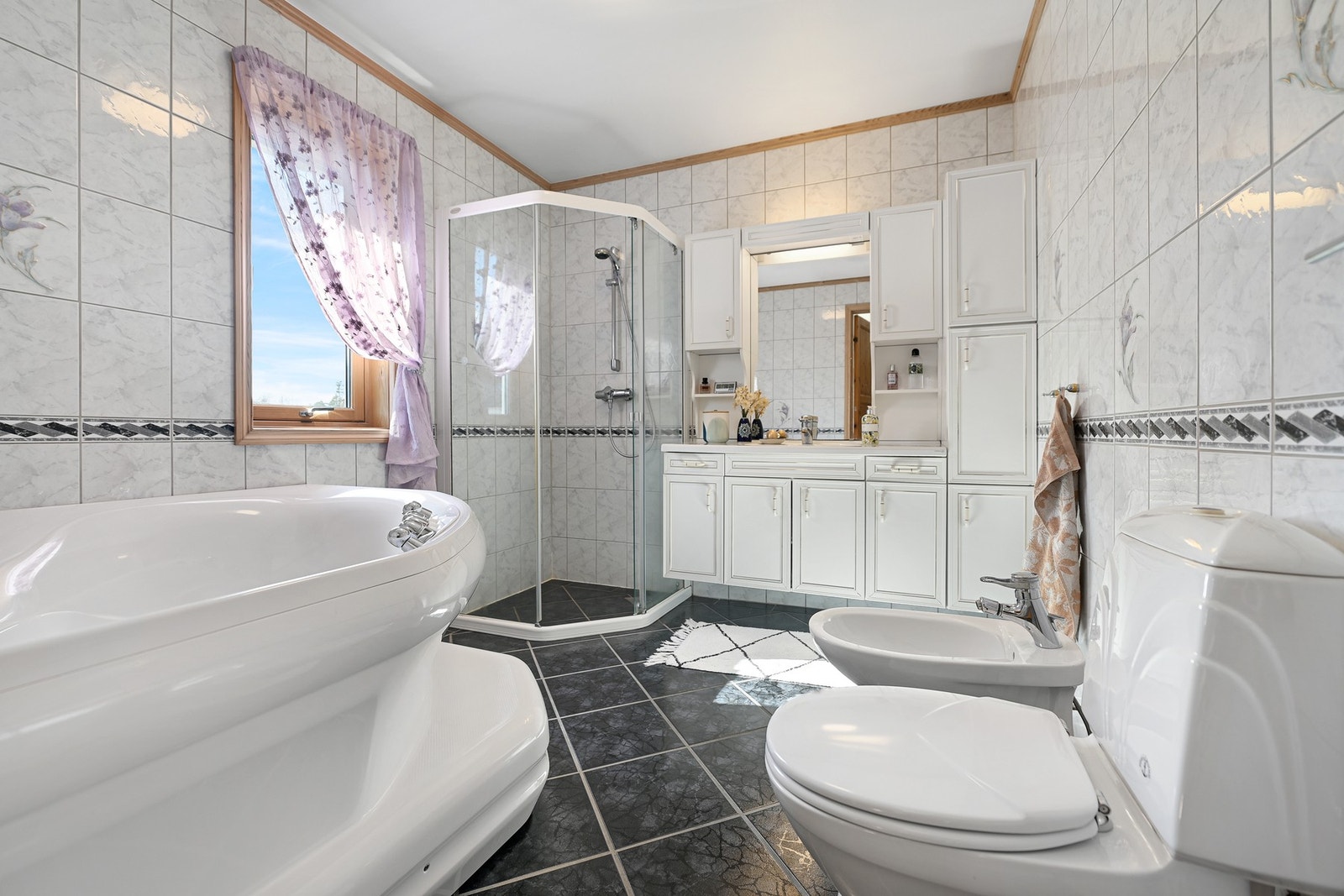 Badet i 1. etasje har adkomst fra hovedsoverommet og er innredet med nedfelt servant, gulvstående toalett, bidé, dusjhjørne og badekar. Galleribilde