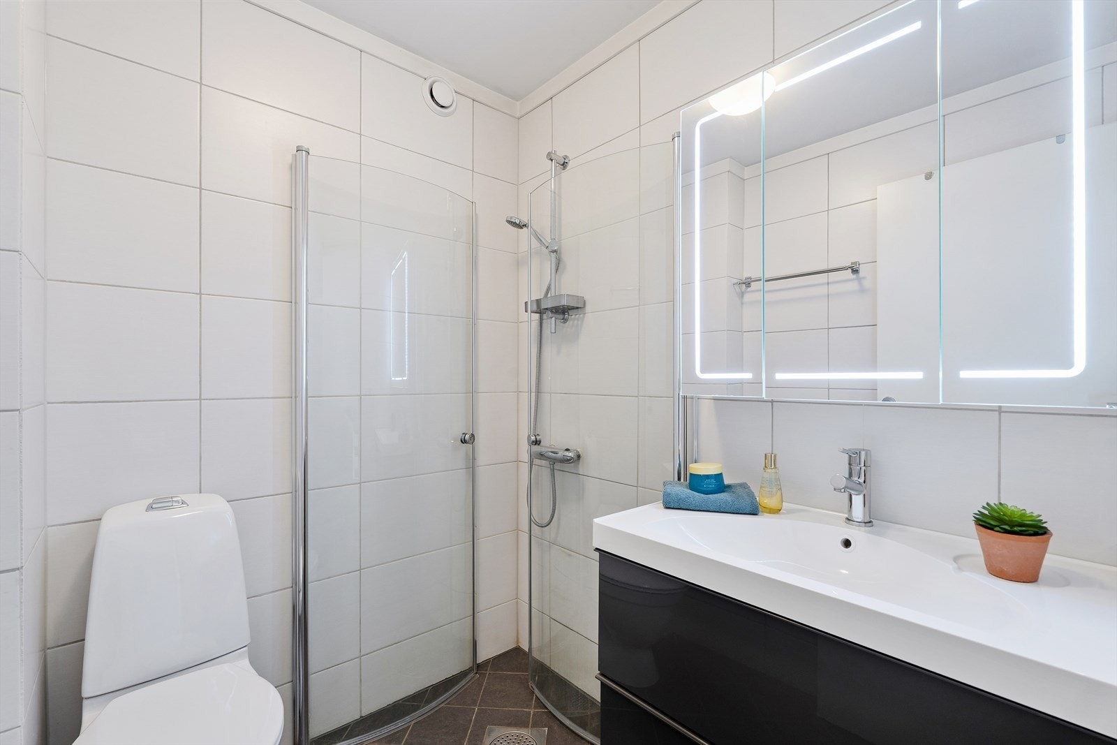 Flislagt bad i første etasje fra 2014 bestående av dusjnisje, toalett og baderomsinnredning - Rikelig med lys i vegghengt speilskap Galleribilde