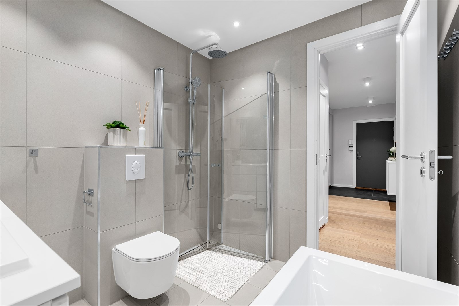 Nedsenket dusjhjørne med glassdører, regndusj og hånddusj samt innebygget badekar. Vegghengt wc med innebygget sisterne. Galleribilde