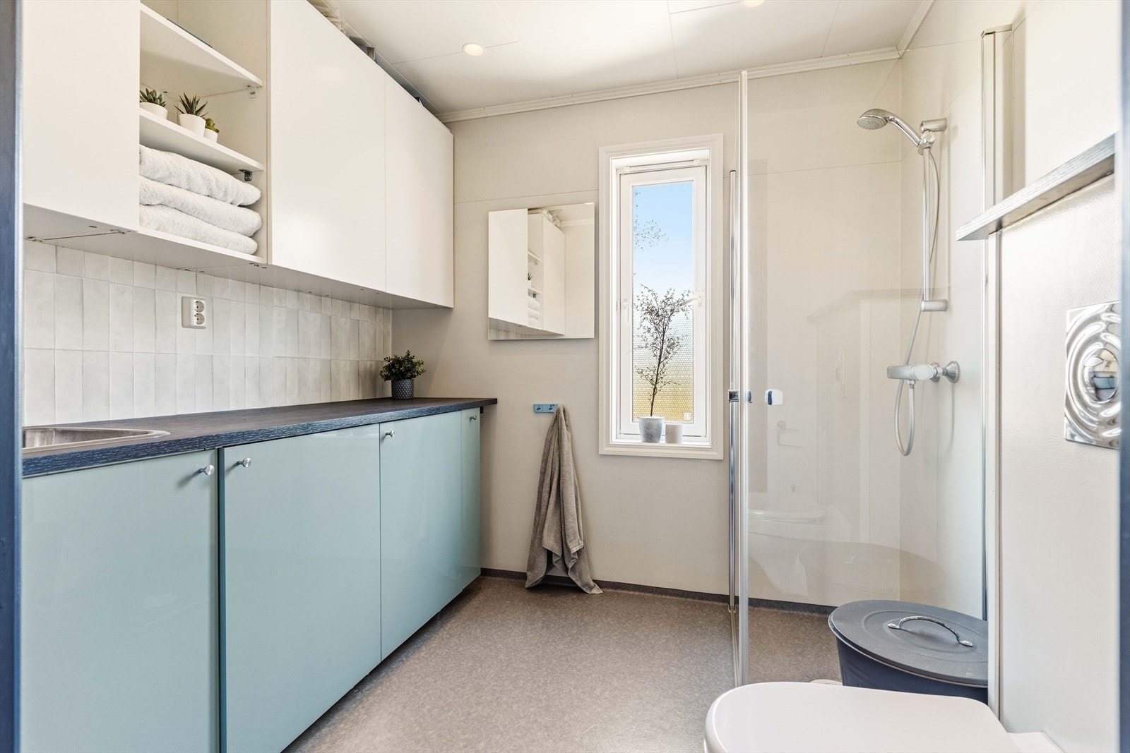 Baderom med dusjhjørne med innfellbare glassdører og vegghengt toalett, samt godt med oppbevaringsplass. Galleribilde