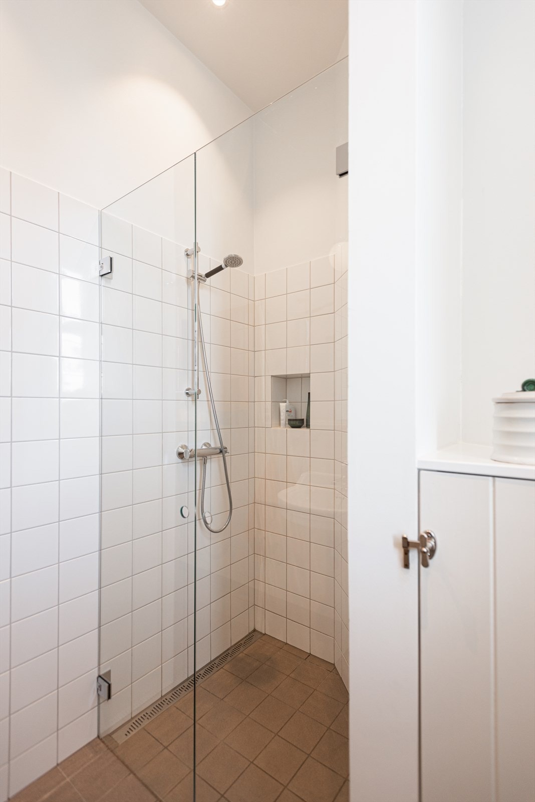 Innredningen består av to innebygde skap med profilerte fronter, dusj med innfellbare dører i herdet glass, servant med speil og belysning over, samt vegghengt klosett med innebygget sisterne Galleribilde