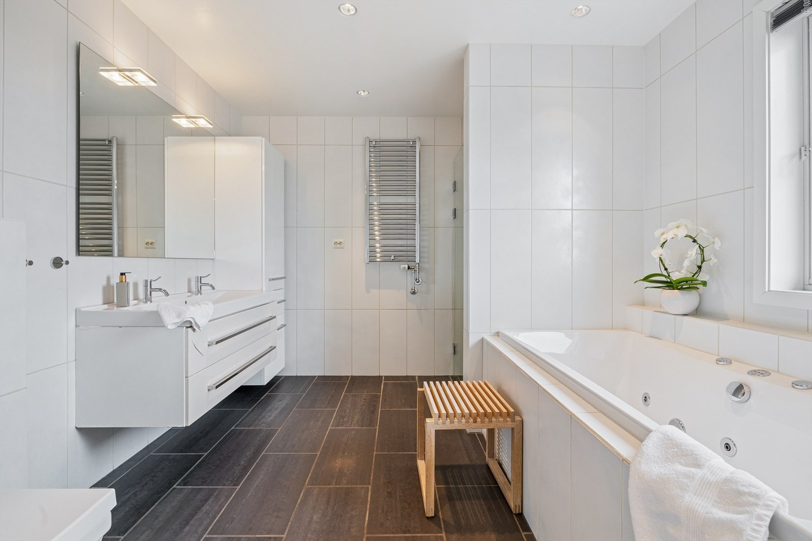 Pent bad med fliser på vegger og gulv med gulvvarme. Badet er utstyrt med baderomsinnredning med dobbelservant, høyskap, dusjnisje, vegghengt toalett og badekar. Galleribilde