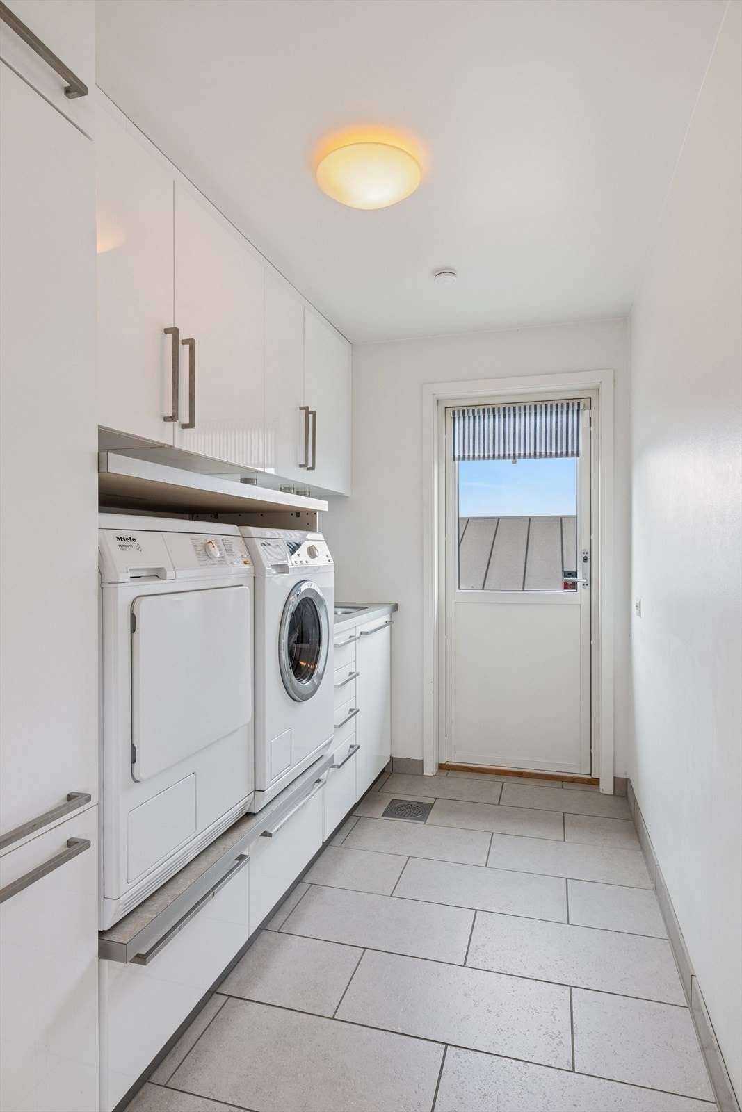 Separat vaskerom med fliser på gulv og malte vegger. Vaskerommet har utslagsvask, opplegg til vaskemaskin og tørketrommel samt godt med oppbevaringsplass. Det er også direkte adkomst ut fra vaskerommet. Galleribilde