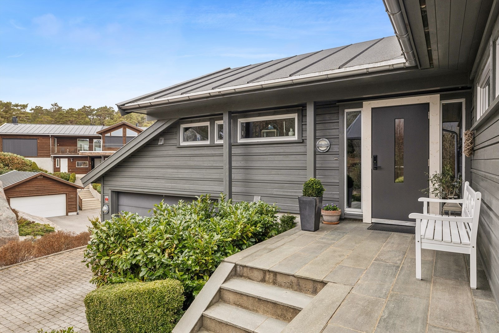 Eiendommen er pent opparbeidet med støttemurer i naturstein og beplantning som rammer inn inngangspartiet. Galleribilde