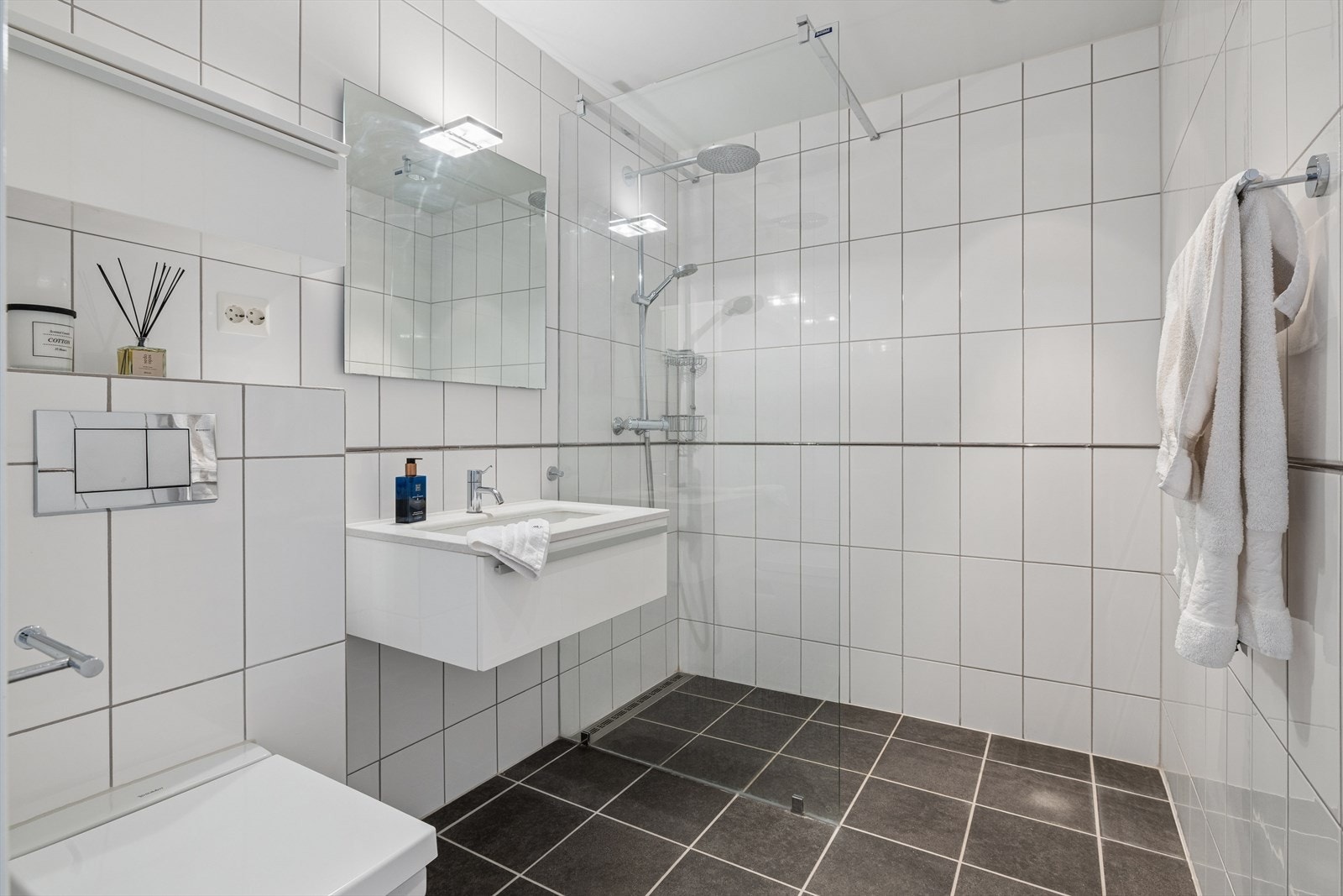 Boligens andre bad har fliser på vegger og gulv med gulvvarme. Badet er utstyrt med baderomsmøbel med servant, dusjnisje og vegghengt toalett. Galleribilde