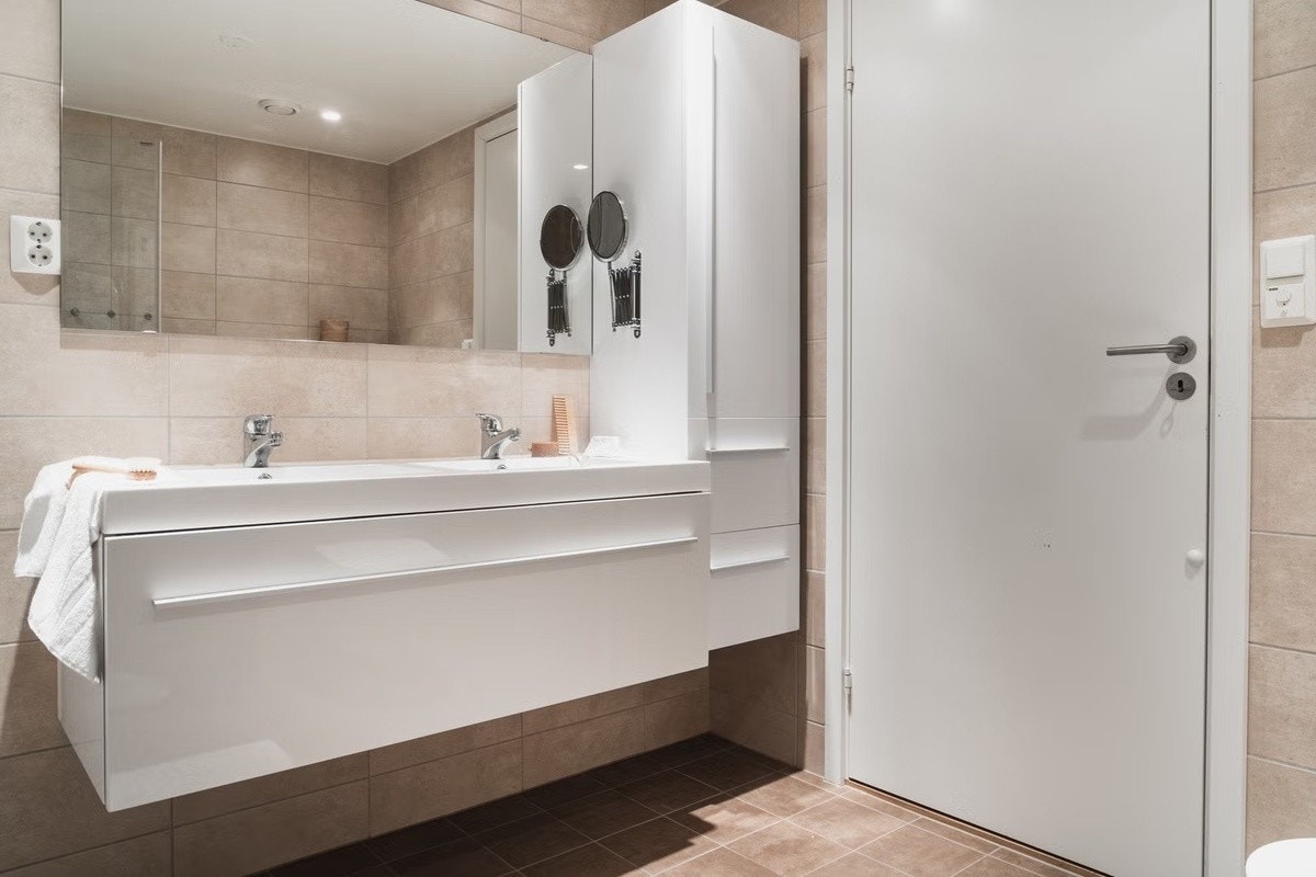Badet inneholder dusjnisje med glassdør, vegghengt toalett og baderomsinnredning med heldekkende dobbel servant og speil. Galleribilde