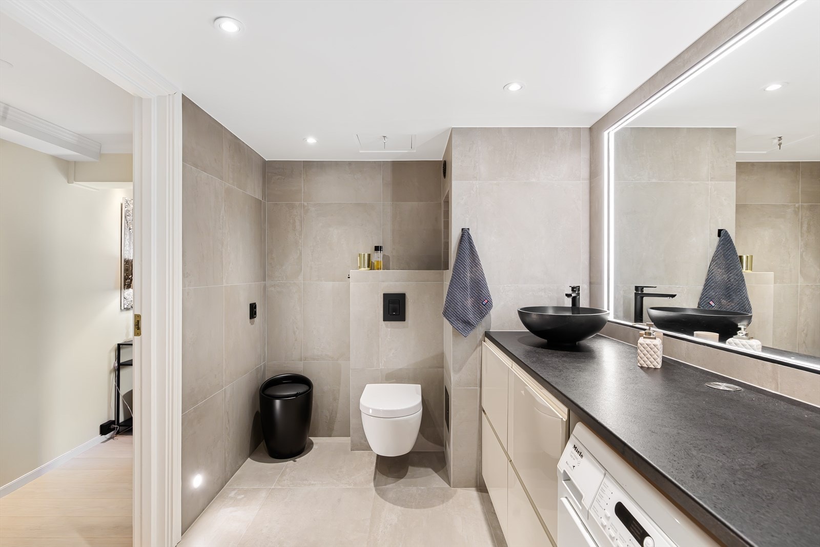 Videre er badet innredet med veggmontert WC, servant med ettgreps blandebatteri samt opplegg for vaskemaskin og tørketrommel under benkeplate. Galleribilde