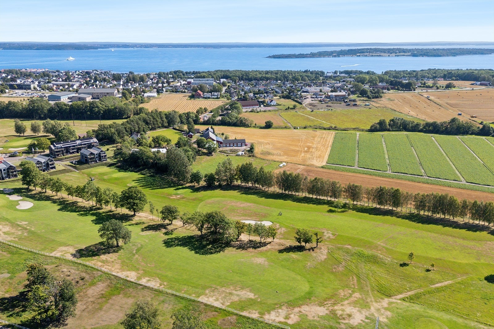 Dronebilde av området med golfbaner, leilighetene til venstre i bildet, og fjorden i bakgrunn Galleribilde