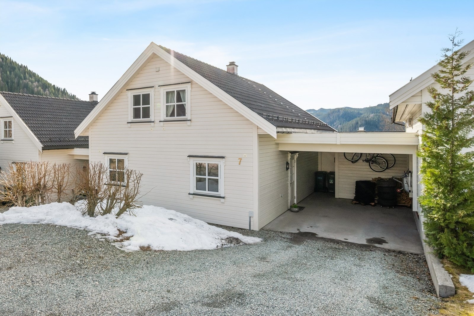 Ved inngangspartiet finner du egen carport med støpt dekke, gruslagt gårdplass, litt plen og frodige prydbusker. Galleribilde