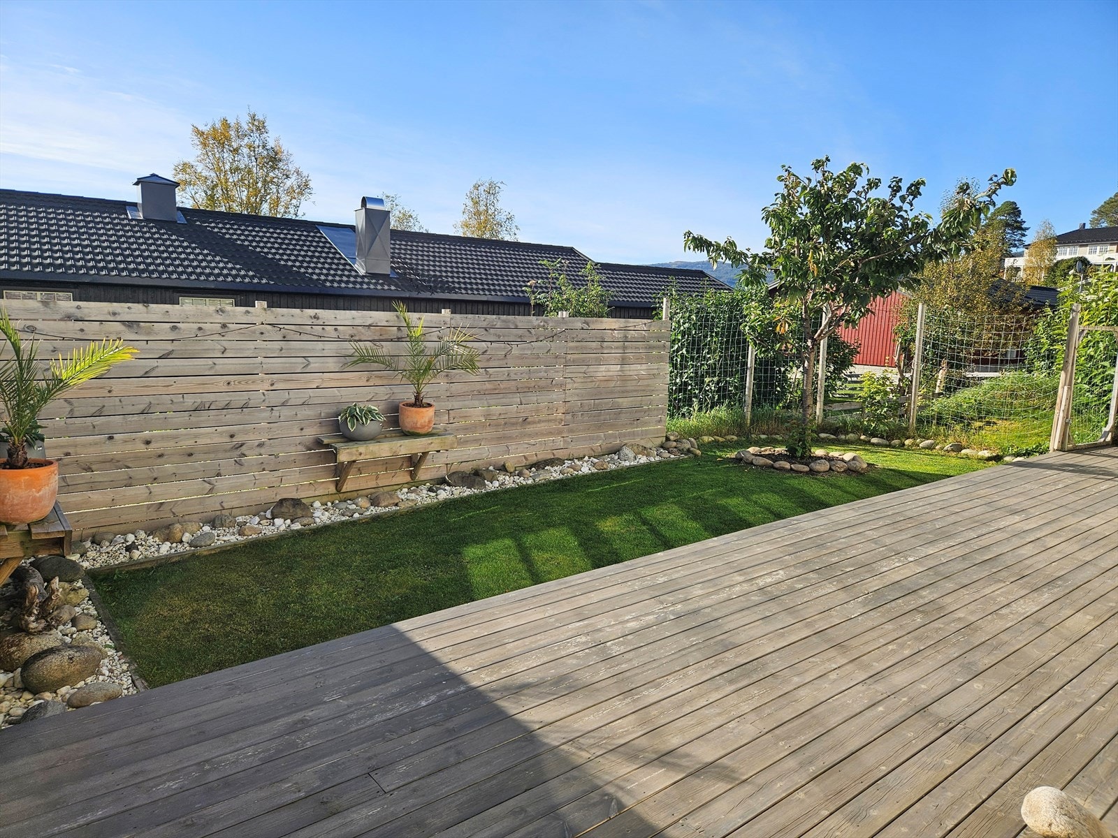 Bilde fra terrassen/hagen på sommeren, tatt av selger. De høye leveggene sørger for at den sydvendte uteplassen er skjermet og privat. Galleribilde