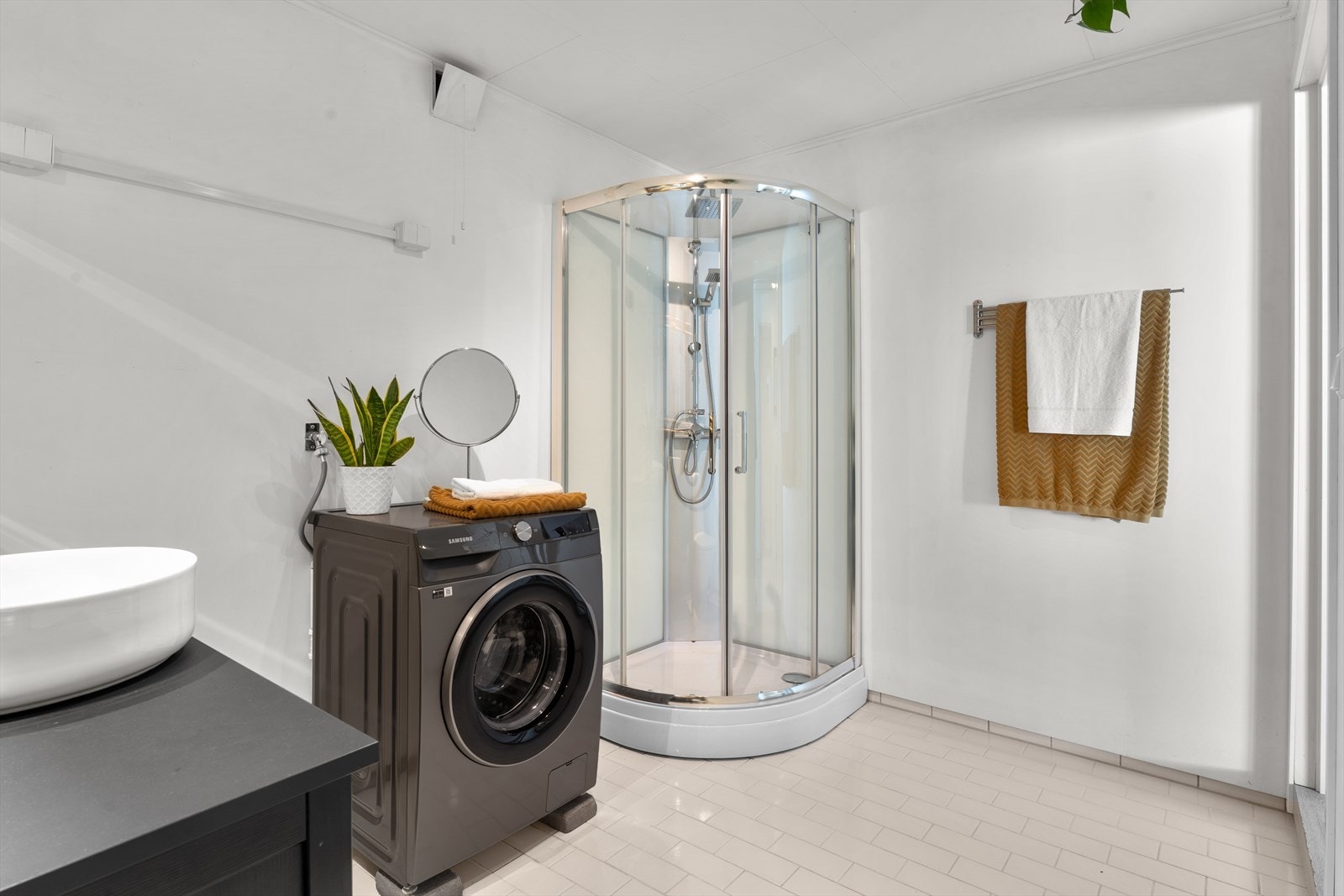 Dusjkabinett med skyvedører, dusjutstyr og regnfallsdusj. Rommet har opplegg og plass for vaskemaskin. Galleribilde