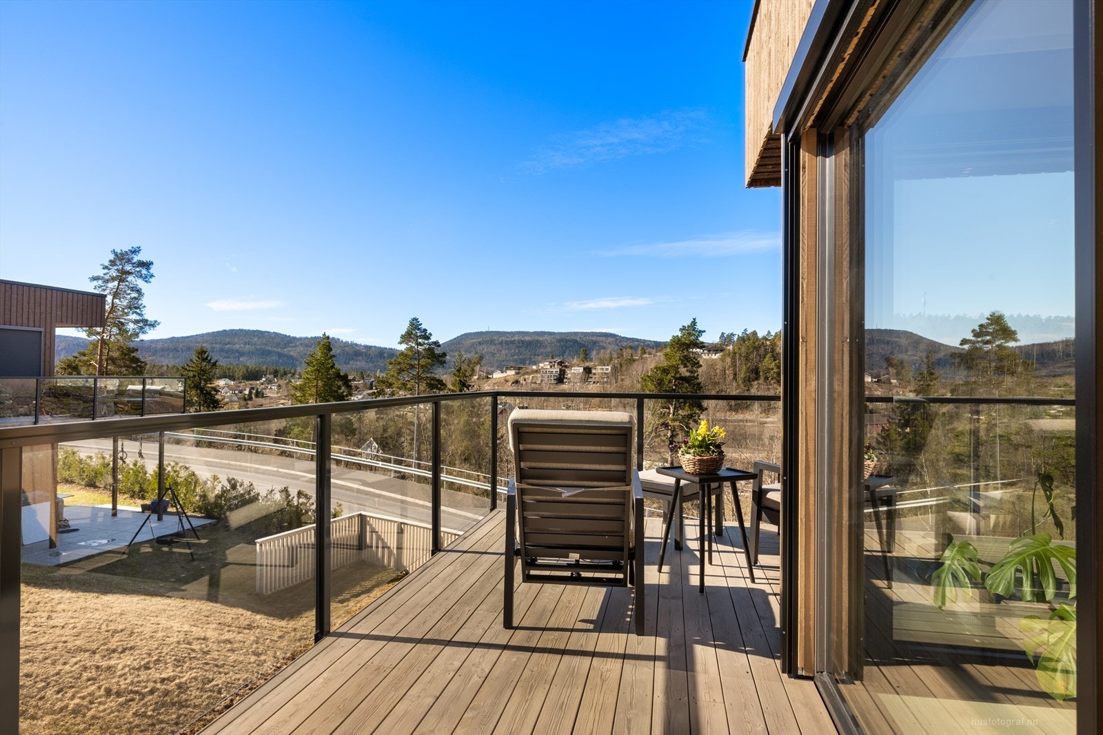 Moderne terrasse med glassrekkverk, solrik utsikt mot naturskjønne omgivelser. Perfekt for avslapning og sosiale sammenkomster i fredelige omgivelser. Galleribilde