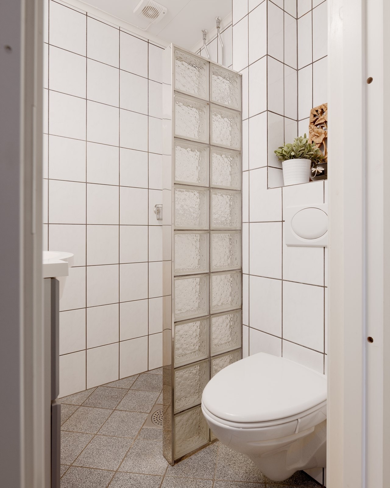 Badet har veggmontert toalett, dusjhjørne med glassbyggerstein og heldekkende servant med underskap. Galleribilde