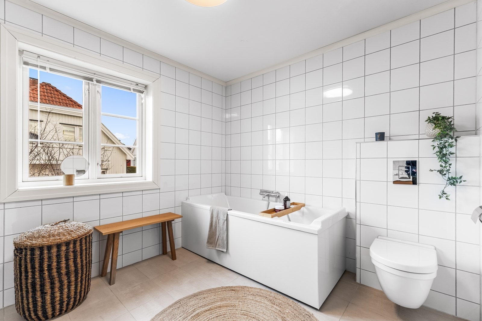 Badet fremstår som romslig og delikat, med flislagte overflater, dusjnisje med glassfelt, regnfallsdusj, badekar, vegghengt klosett og en praktisk servantinnredning med dobbel servant. Galleribilde