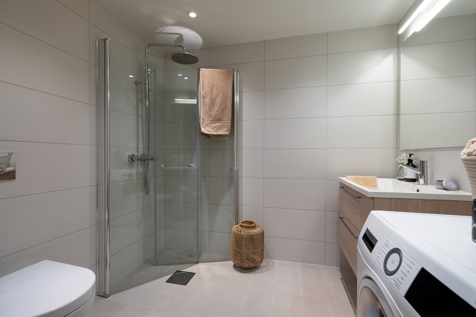 Badet er av meget god størrelse og er utstyrt med innredning med to skap og nedfelt servant, samt speil med belysning over. Videre er det vegghengt toalett, skap og dusjvegger/hjørne som frigjør plass på gulvet. Galleribilde