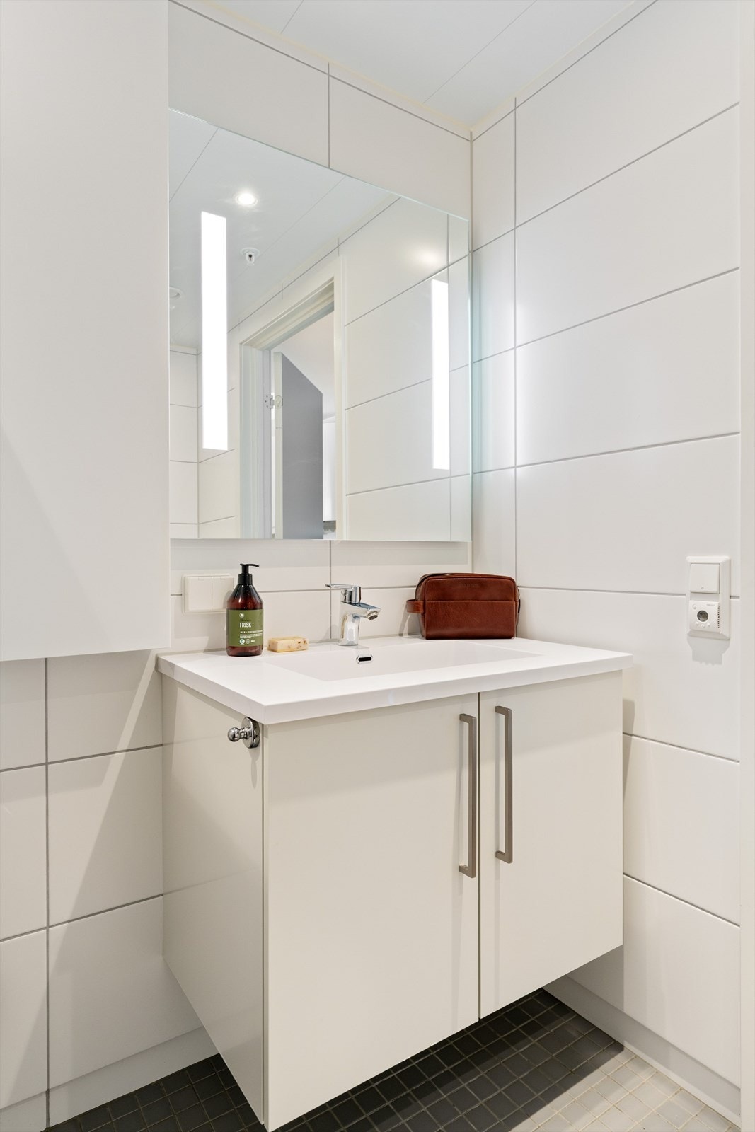 Badet er utstyrt med vegghengt toalett, dusjhjørne med innfellbare glassdører, speil og opplegg for vaskemaskin. Galleribilde