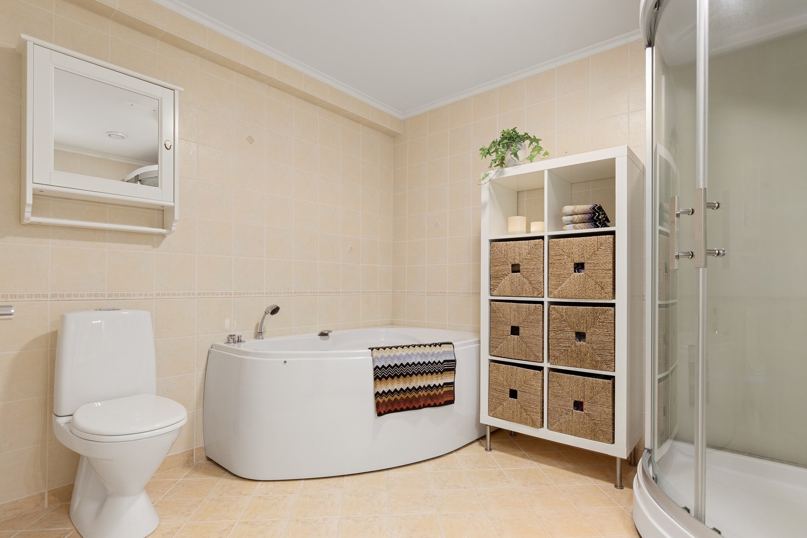 Lyst flislagt bad med gulvvarme i underetasje. Badet er innredet med badekar, steamdusj, gulvstående toalett og servantskap med speil og belysning Galleribilde