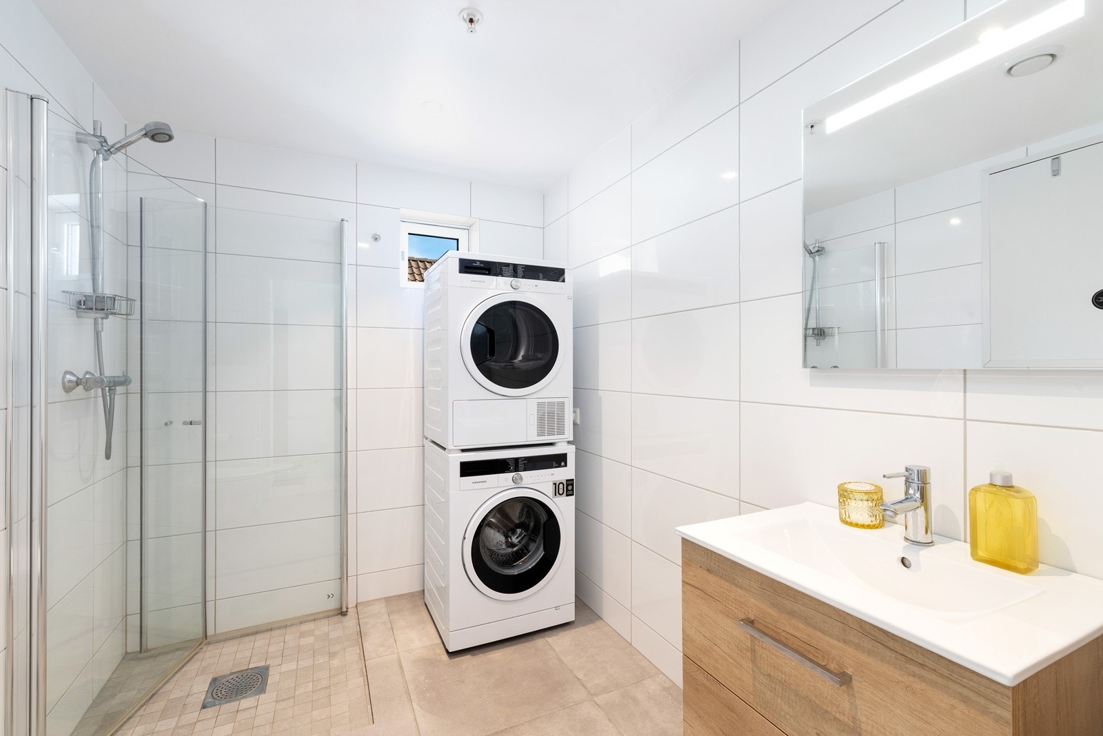 Pent flislagt bad med varme i gulv. Badet har dusjhjørne, veggehengt toalett, servant med underskuffer samt opplegg til vaskemaskin og tørketrommel. Galleribilde