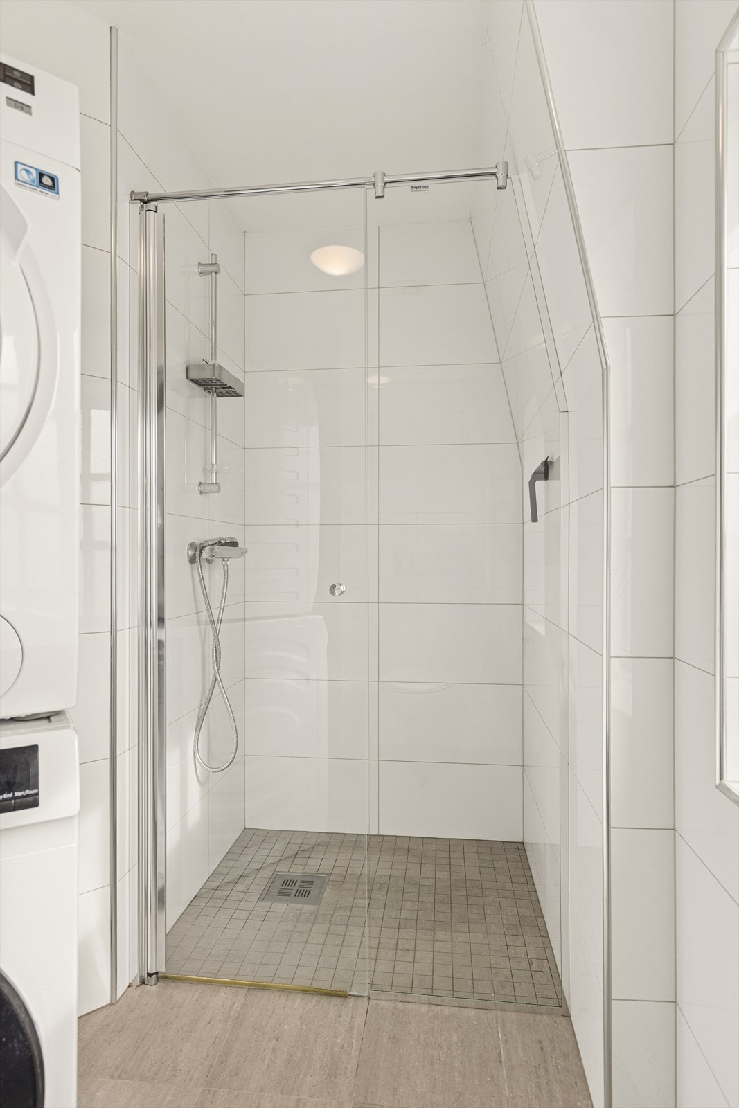 Badet er fra 2015 og har dusjnisje, servantseksjon, veggmontert toalett, fordelerskap for vannrør og opplegg for vaskemaskin. Galleribilde