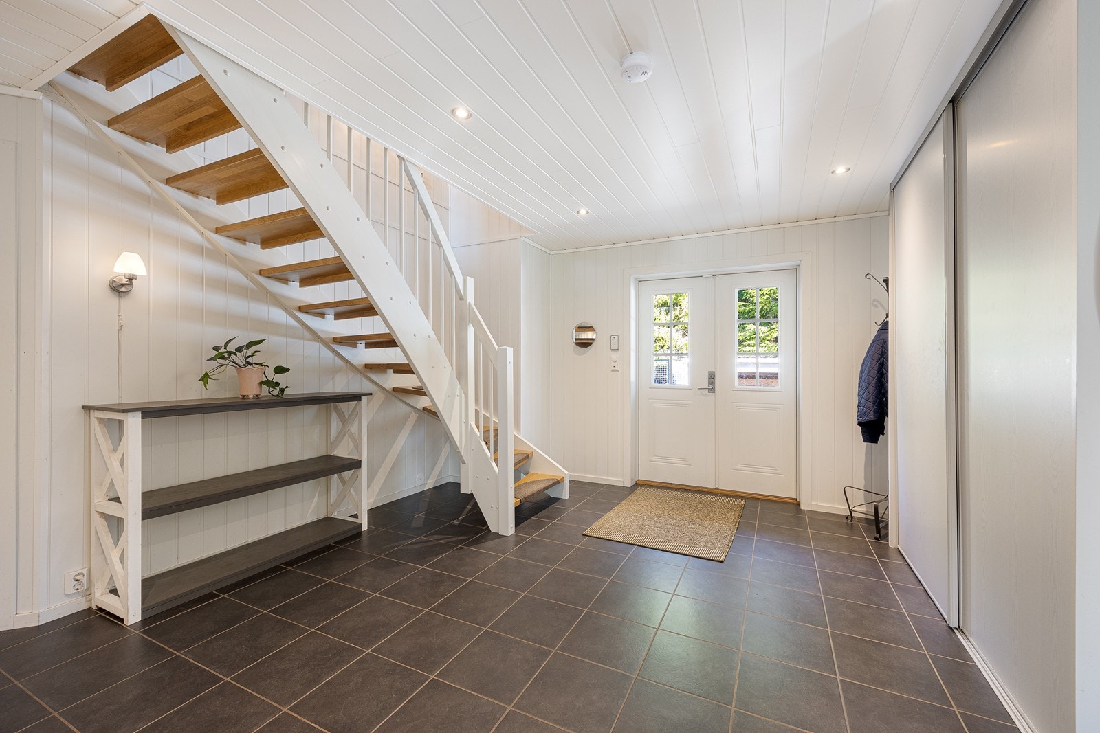 Vel inne har boligen en bred og tiltalende hall med downlights, gråmalte panelplater og varme under grå gulvfliser. Galleribilde