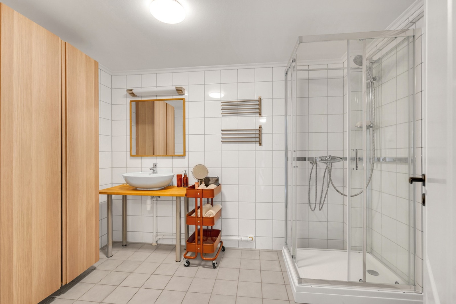 Lyst og helfliset bad med gulvvarme utstyrt med dusjkabinett, gulvmontert toalett, benk med servant, rørskap og opplegg for vaskemaskin. Galleribilde