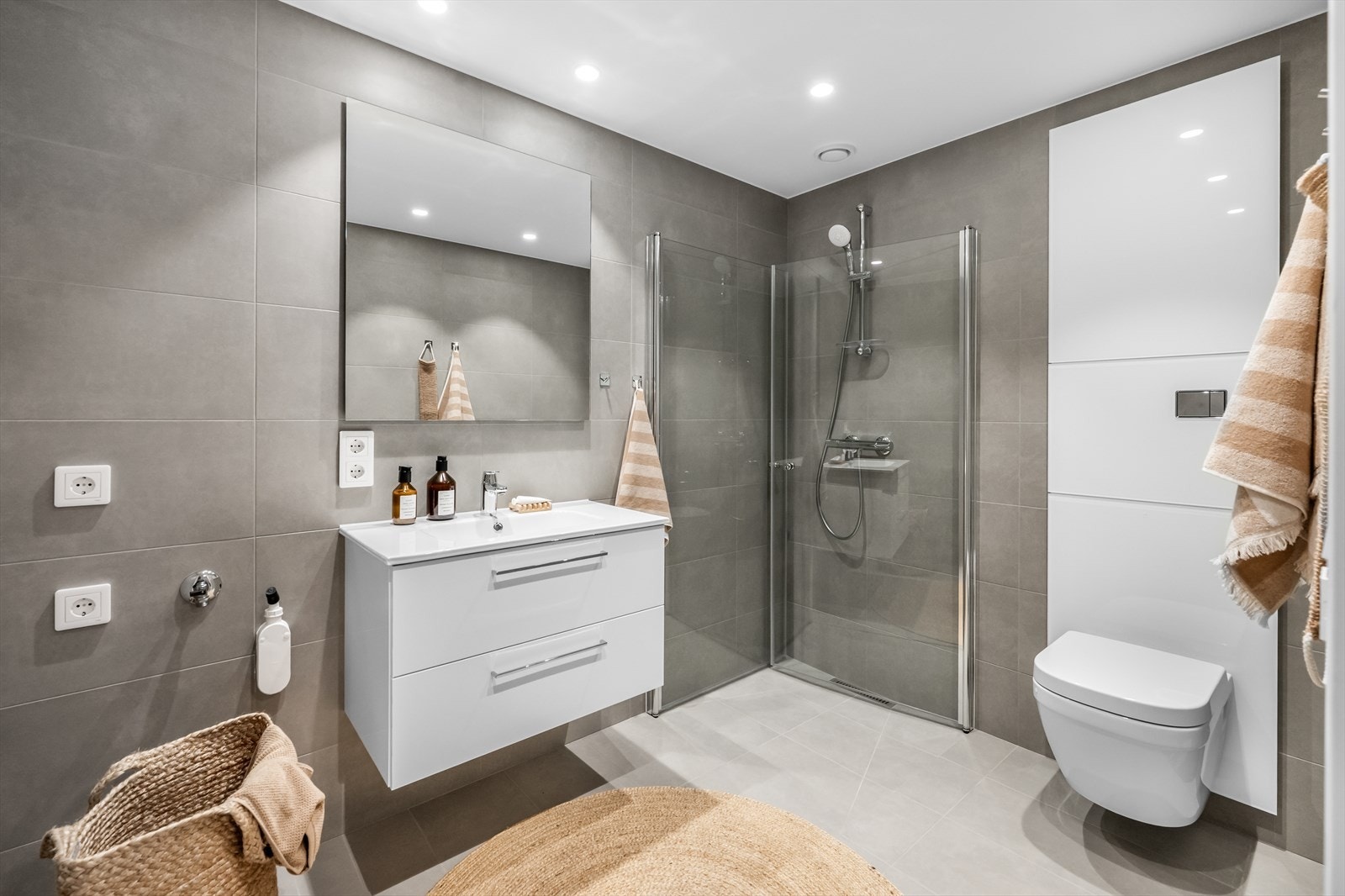 Badet er utstyrt med vegghengt toalett, dusj, servant med underskuffer, vegghengt speil og opplegg til vaskemaskin. Galleribilde