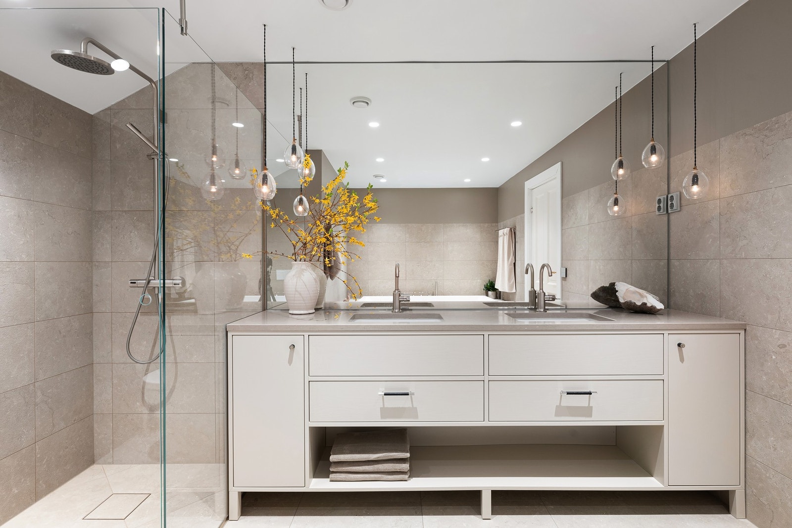 Et lyst og moderne bad med dobbel servant, store speil og dusjhjørne i glass, innredet i nøytrale toner og elegante detaljer. Galleribilde