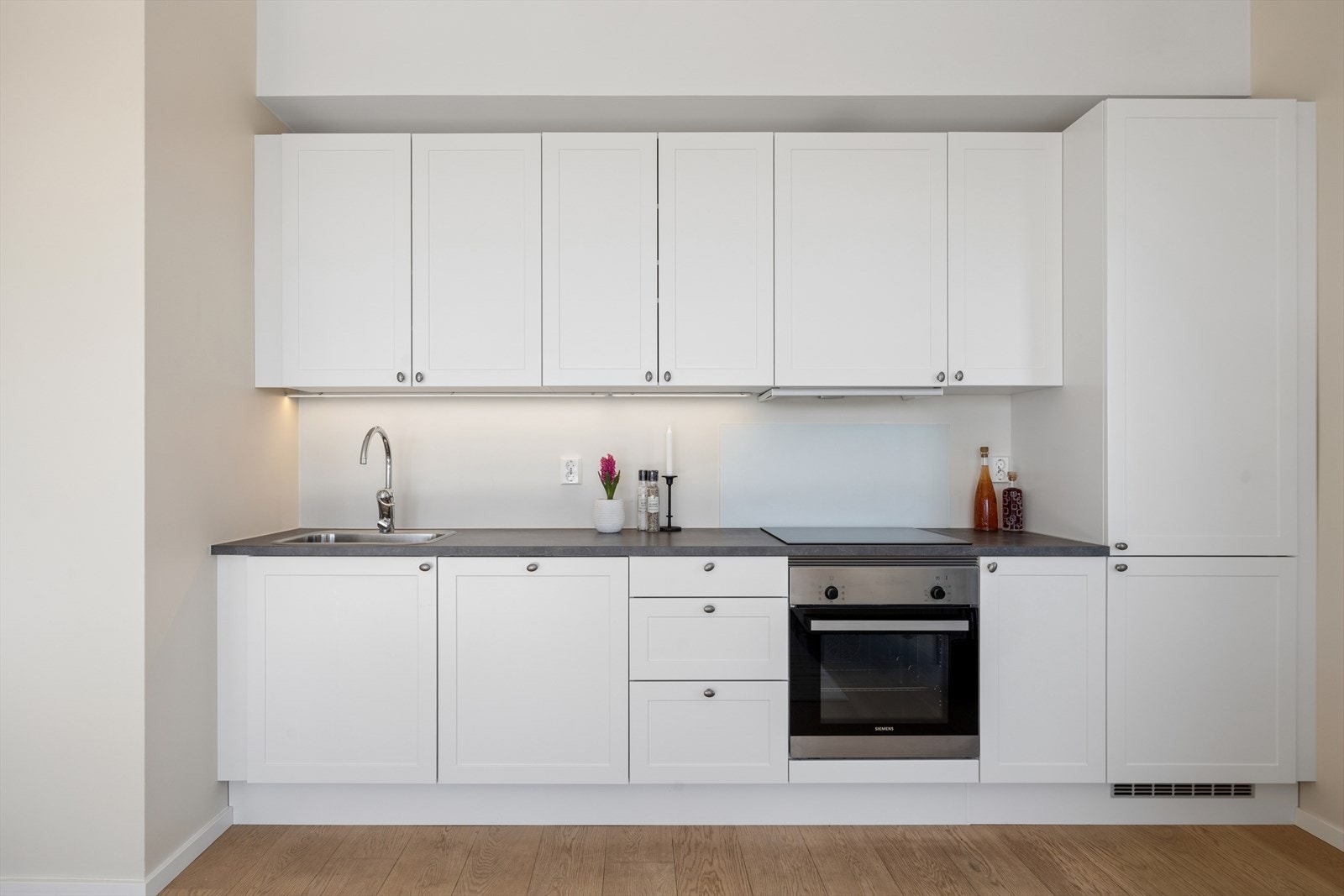 innbydende HTH-kjøkkenet har innredning med hvite, profilerte fronter, laminat benkeplate og planlimt kum i rustfritt stål. Galleribilde