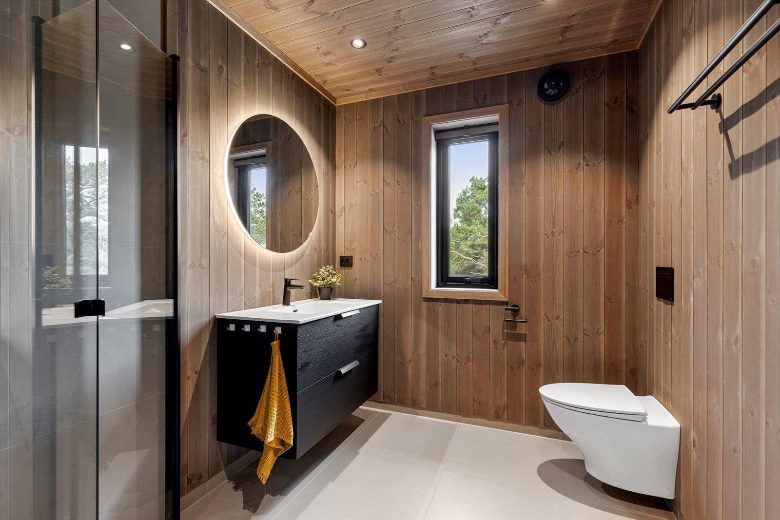 Badet er utført med flislagt gulv, vegghengt toalett og panel på vegger og i tak. Galleribilde