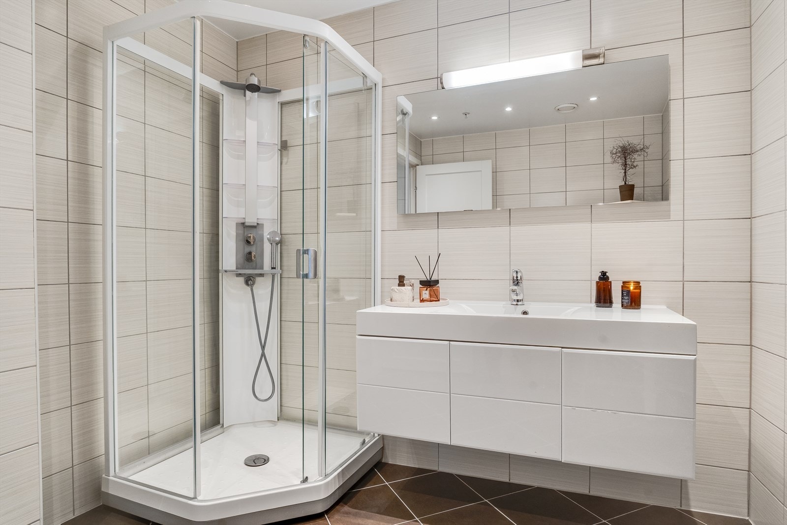 Flislagt bad, innredet med nedfelt servant, veggmontert toalett, speil og dusjkabinett Galleribilde