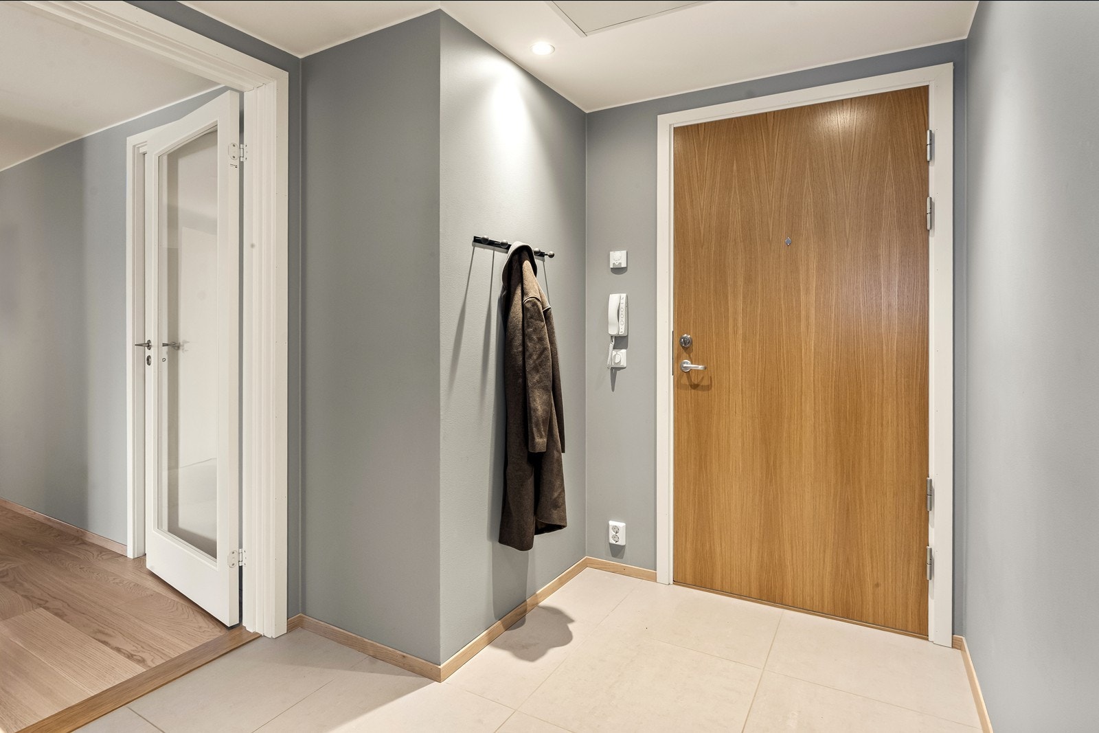 Vel inne blir vi ønsket velkommen i en pen entré med glatte vegger, downlights i himlingen og store, grå fliser på gulv med vannbåren gulvvarme. Galleribilde