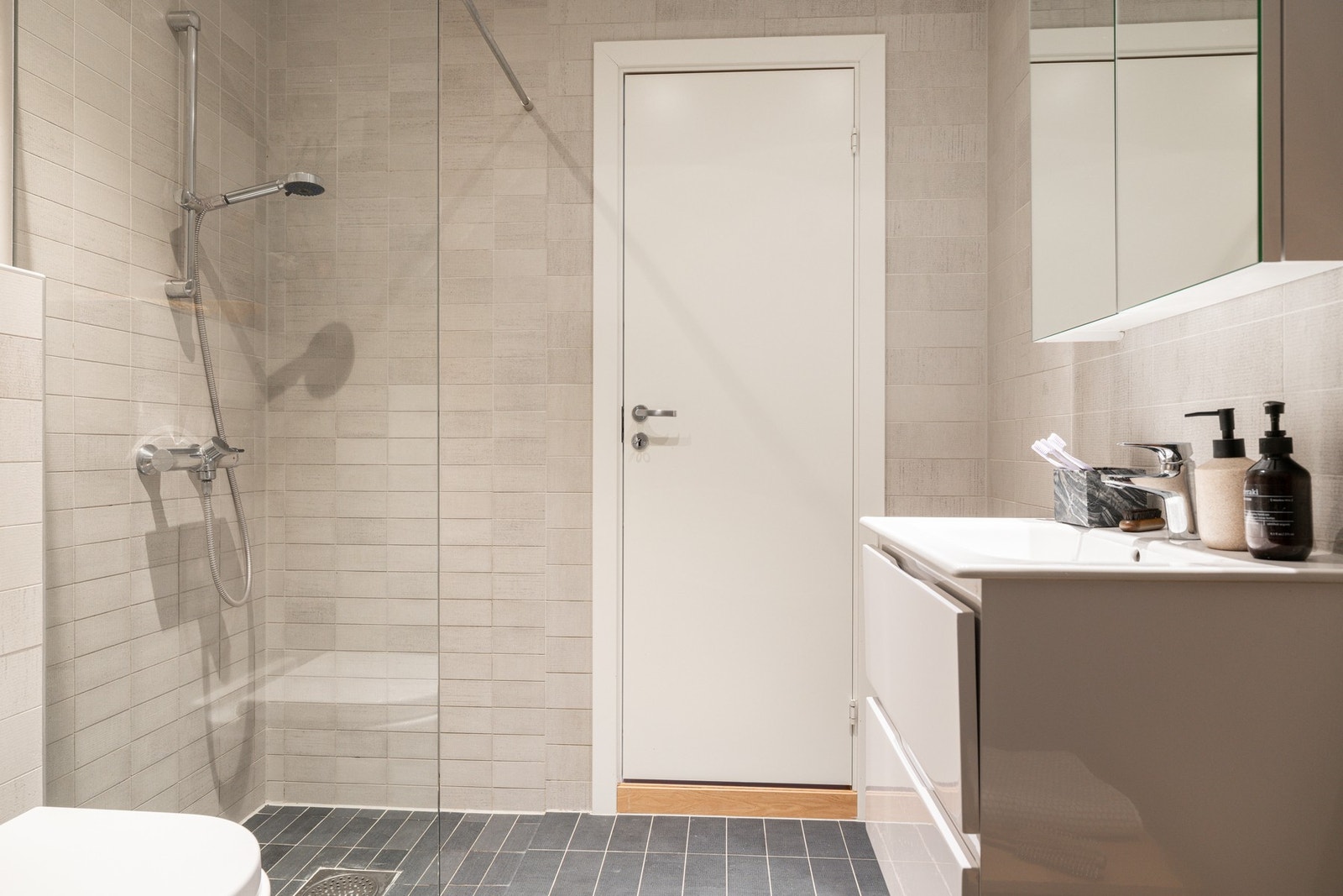 Badet er utstyrt med servant med innredning, dusjhjørne med glassvegg og vegghengt toalett Galleribilde