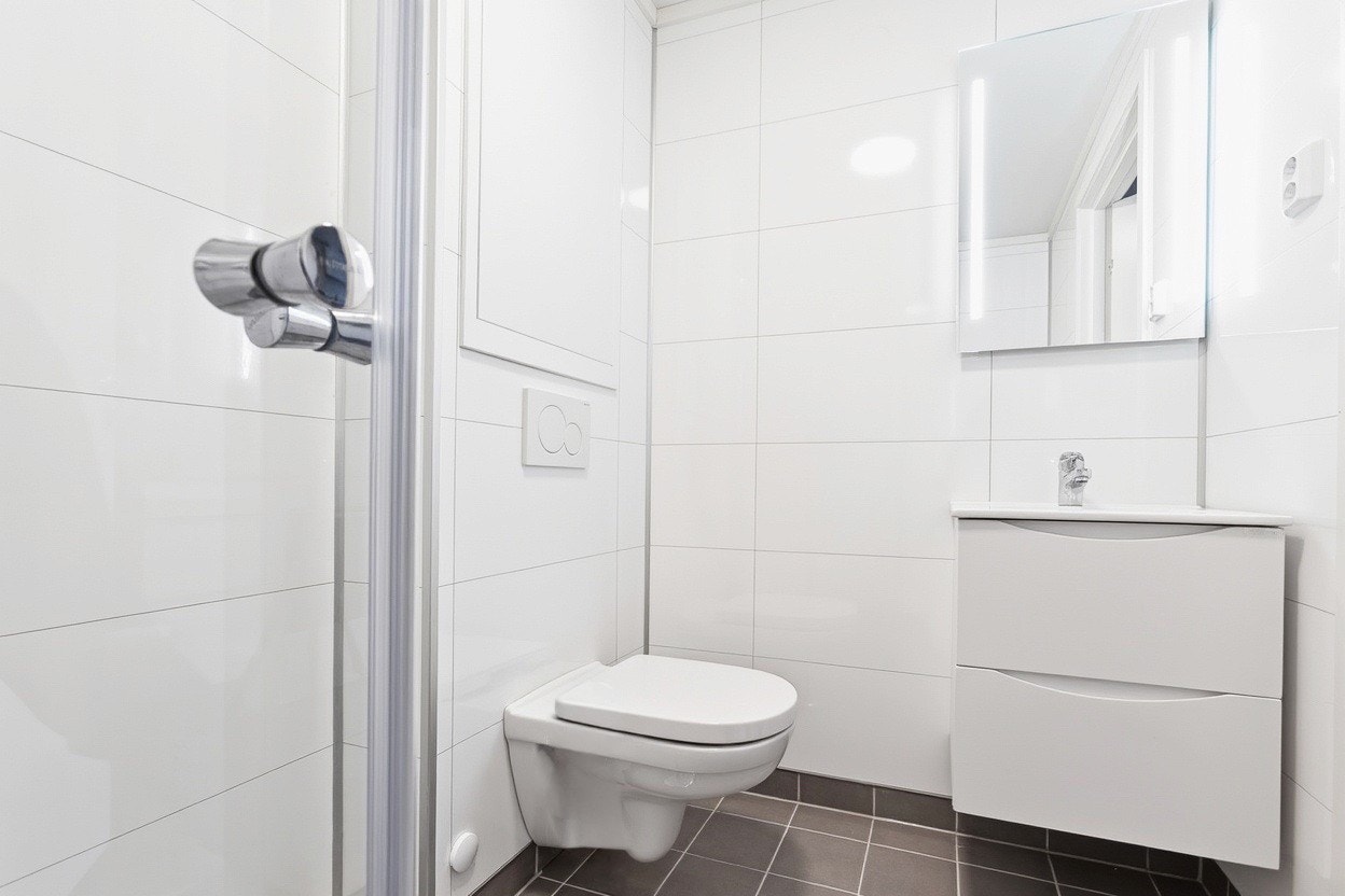 Badet har vegghengt toalett og servant med speilskap Galleribilde