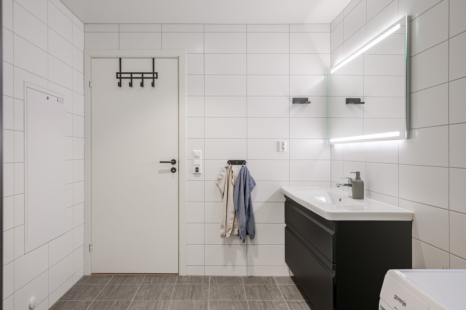 Baderommet har grå fliser på gulv med elektriske varmekabler under, hvite fliser på veggene, downlights i himlingen og avtrekk via balansert ventilasjon. Galleribilde