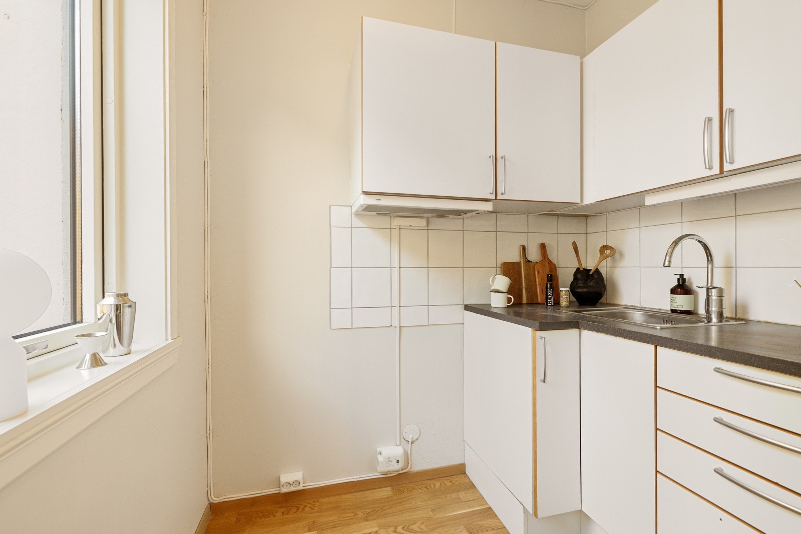 Tvis-kjøkkeninnredning fra 2020 med glatte hvite fronter, grå laminatbenkeplate med nedfelt vaskekum i børstet stål og ettgreps krummet armatur Galleribilde
