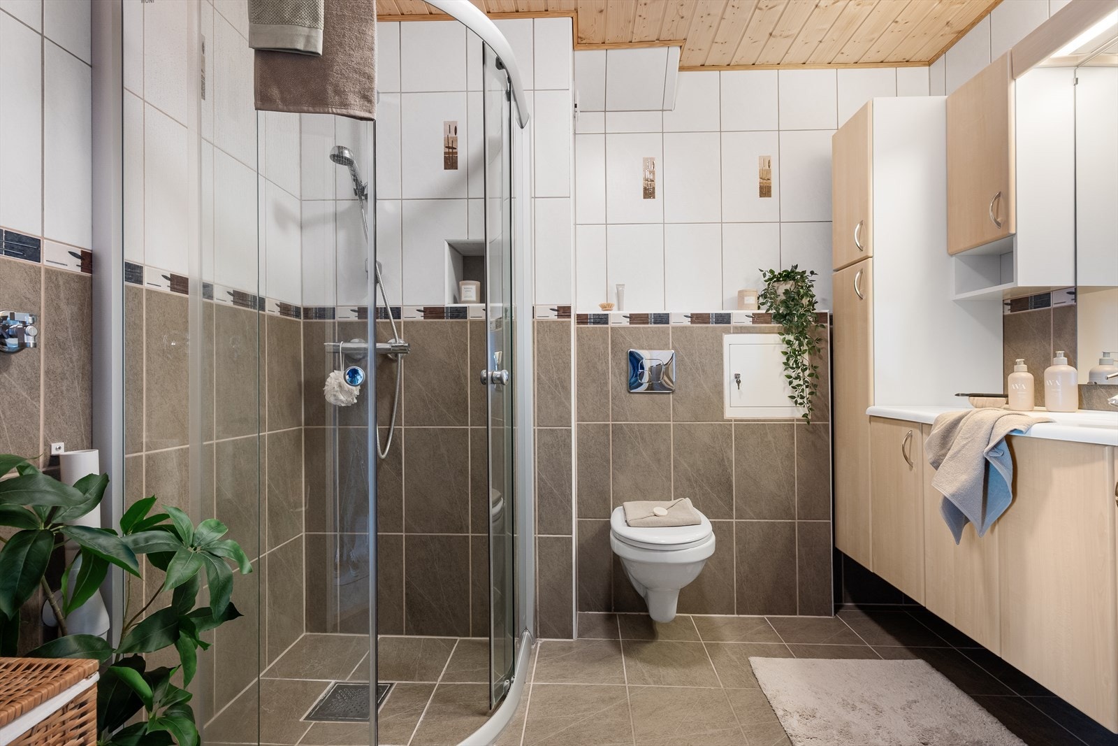Flislagt bad med vegghengt toalett, dusjvegger og baderomsinnredning med speil og belysning. Varmekabler i gulv. Det er også opplegg for vaskemaskin. Galleribilde