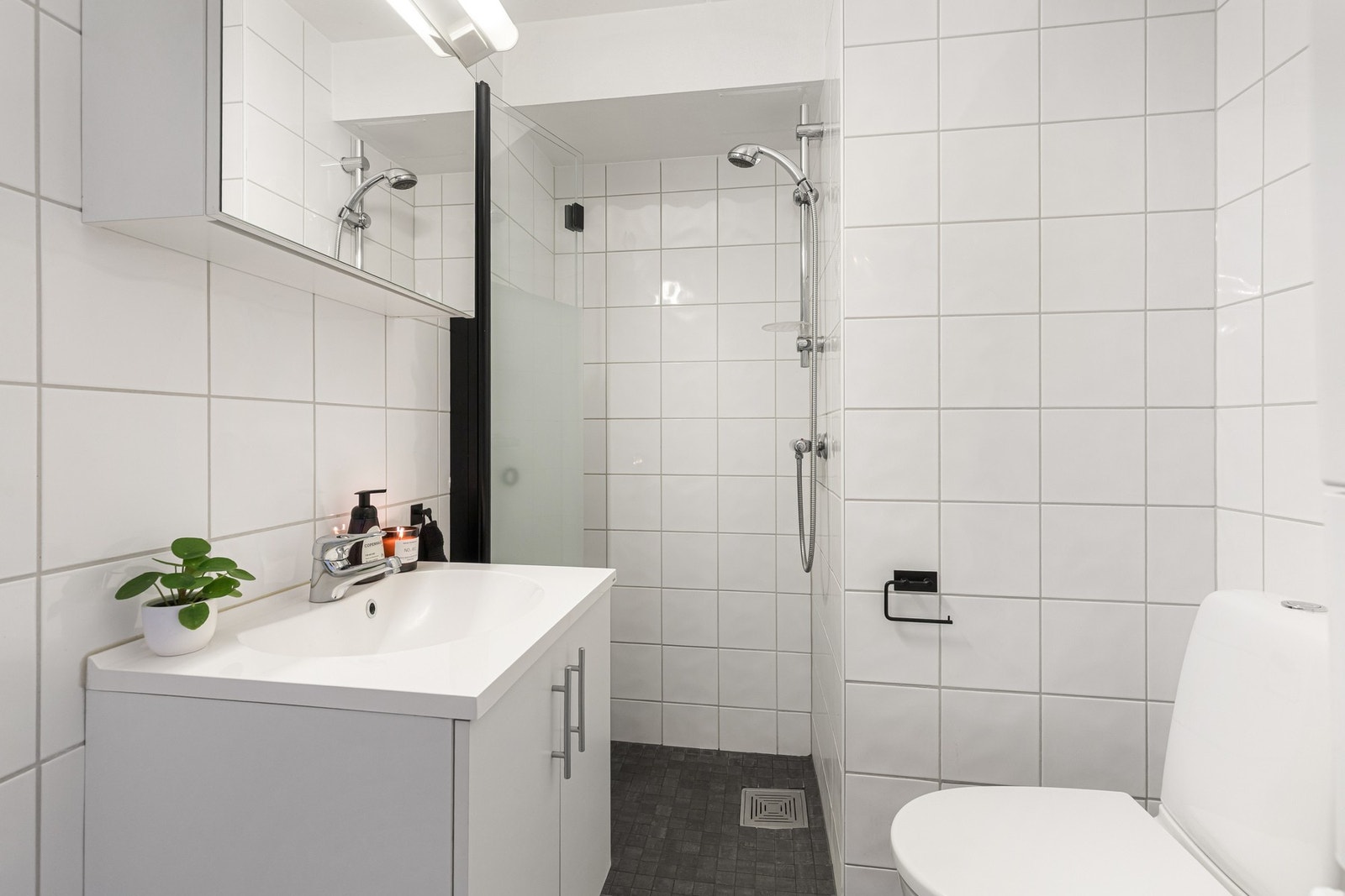 Badet fremstår lyst og pent, med grå fliser på gulv og hvite fliser på veggene. Galleribilde