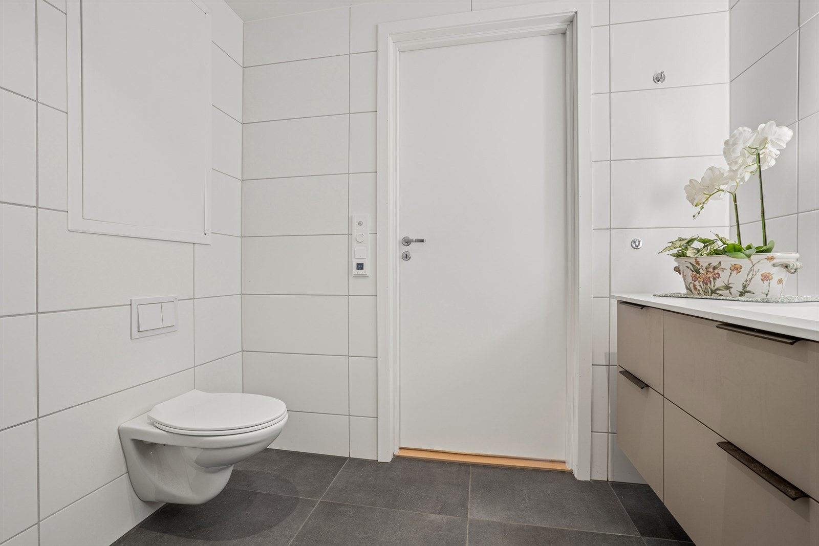 Badet er innredet med dusjvegger av glass og dusjgarnityr på vegg, vegghengt toalett og servant. Opplegg for vaskemaskin. Galleribilde