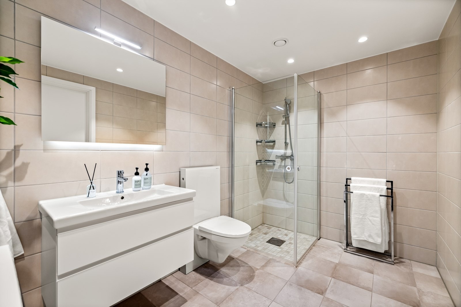 Badet har et tidløst uttrykk med lyse fliser, downlights og hvit innredning. Det er varme i gulvet og balansert ventilasjon. Galleribilde
