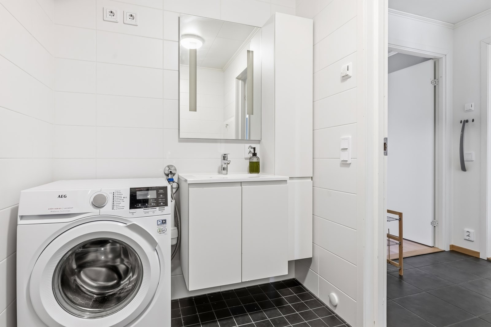 Badet er ellers utstyrt med dusjhjørne med innfellbare dører, vegghengt toalett og baderomsinnredning med nedfelt servant. I tillegg har man opplegg for vaskemaskin. Avtrekk via balansert ventilasjonsanlegg. Galleribilde