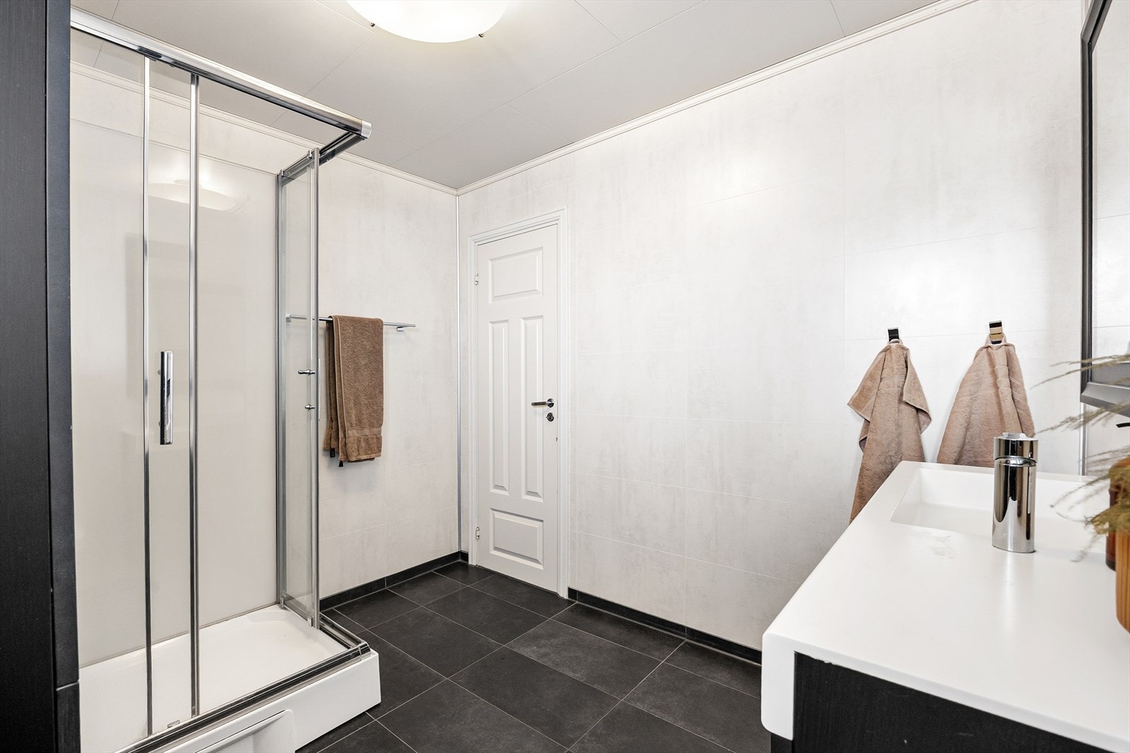 Videre har badet vegghengt toalett, dusjakbinett og lun varme i gulvet under sorte gulvfliser. På veggene er det lysegrå våtromsplater. Galleribilde
