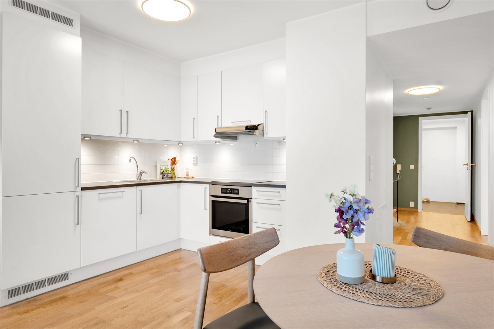 Stilrent kjøkken i hvit utførelse, med integrerte hvitevarer, underskapsbelysning og god oppbevaringsplass i både skuffer og skap. Galleribilde