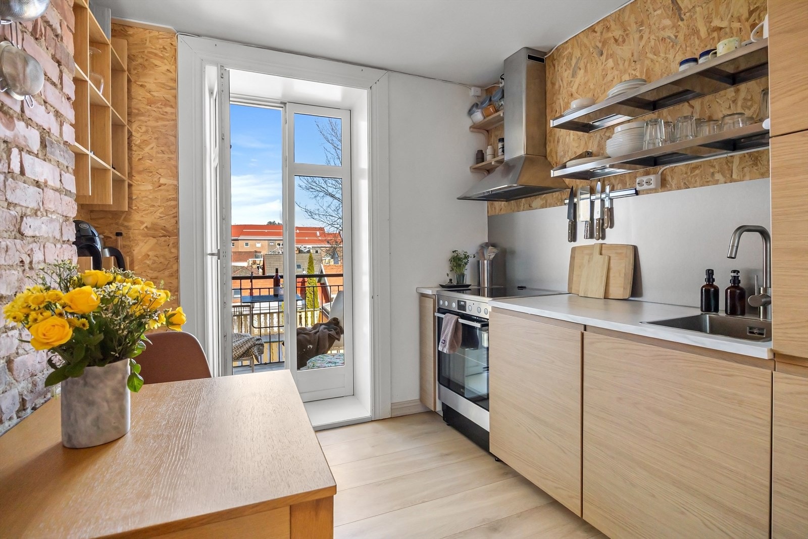 Moderne kjøkken fra 2024 med slette fronter og åpne hyller som gir et luftig uttrykk. Laminat benkeplate med nedfelt kum i rustfritt stål og ett-greps blandebatteri. Integrerte hvitevarer som oppvaskmaskin og kjøleskap bidrar til et helhetlig preg. Galleribilde
