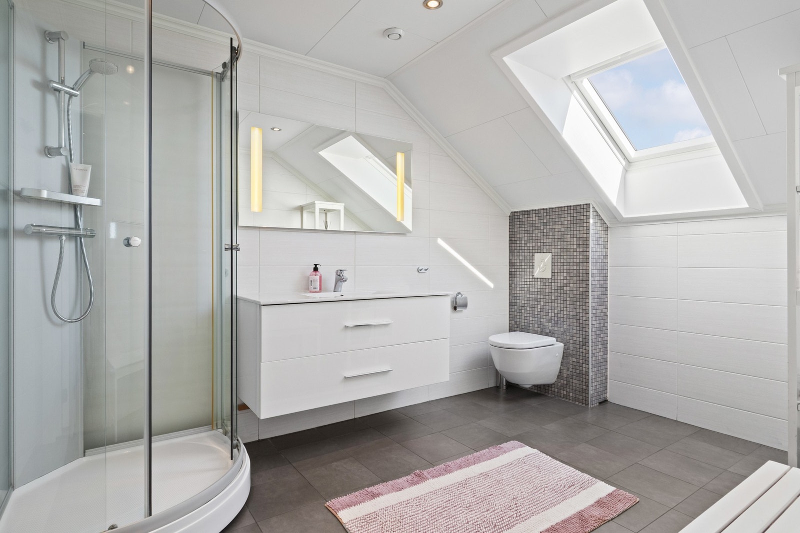 Badet i 2. etasje har flislagt gulv og vegger i lyse og grå toner. Rommet får godt med naturlig lys fra takvindu. Galleribilde